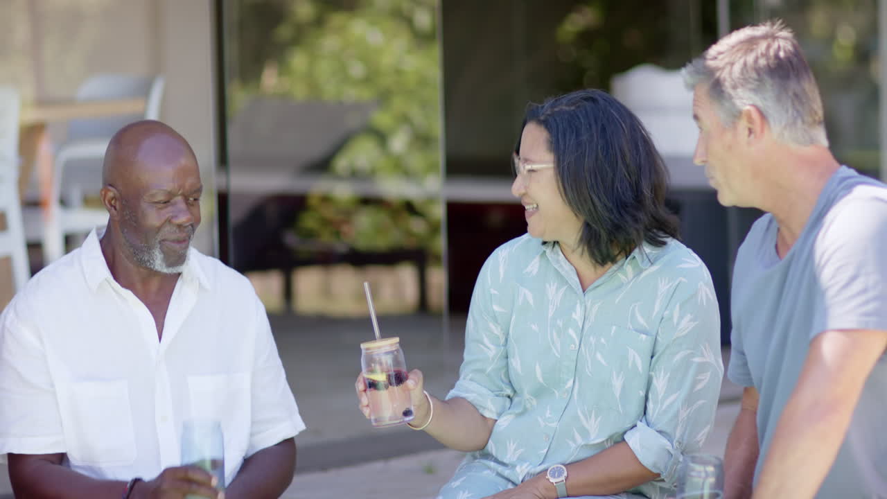 Senior diverse friends sharing drinks and laughter in garden, enjoying conversation together