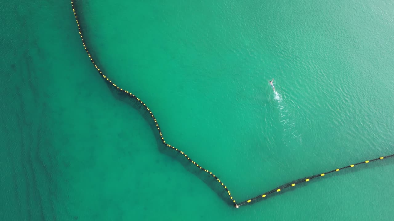 воздух сверху вниз активного пловца, плавающего в охраняемой океанской зоне на пляже куги утром - нисходящий вид сверху