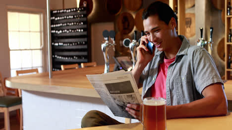 Mann-Spricht-Mit-Dem-Handy,-Während-Er-In-Einem-Restaurant-Zeitung-Liest-4k