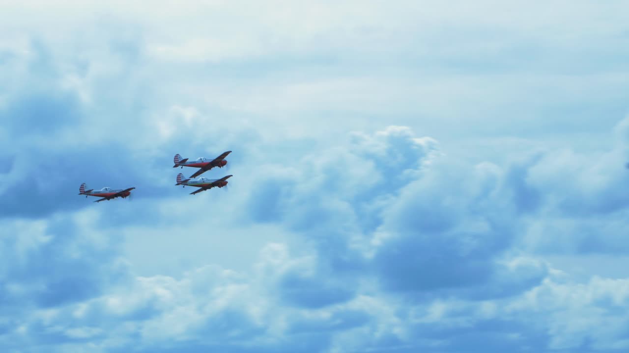 Three red YAK-50s aerobatic aircrafts carrying out dynamic maneuvers in front of spectators at Baltic airshow in Liepaja, Latvia, white smoke trails, handheld shot