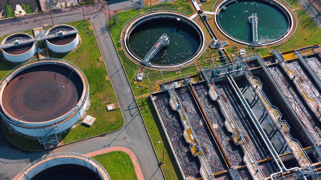 Top view of circular clarifiers and aeration basins in facility. High angle shot of round water tanks and rectangular filtration systems with walkways