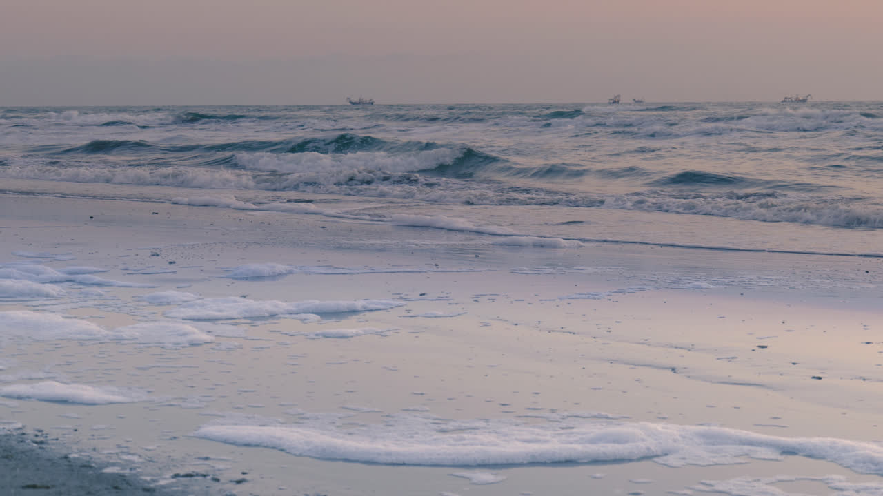파도가 조용히 해가 지는 동안 평화로운 모래 해변을 고 해변을 따라 어져 있는 거품