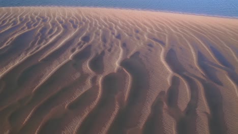 el aumento se revela sobre la arena texturizada hasta un impresionante océano azul en un día soleado