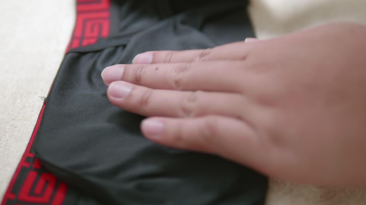 남자의 손은 여행 중 보관을 용이하게 하기 위해 남성용 빨간색 가장자리와 검은색 속옷을 접고 있습니다.