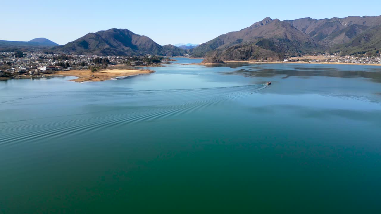 Pemandangan luas Danau Kawaguchi dengan air tenang dan perahu kecil di kejauhan. Lanskap Jepang yang damai, diapit pegunungan dan diterangi cahaya siang yang lembut.