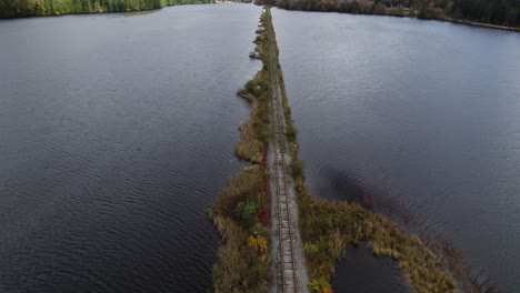 abandoned railway embankment going through lake toward fall forest and hills