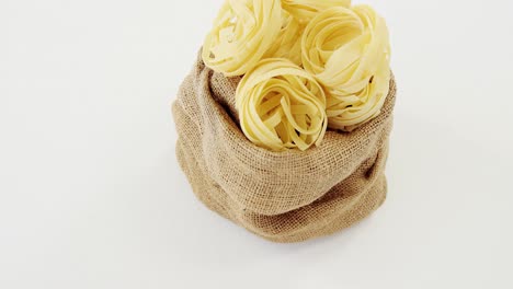 pasta de tagliatelle cruda en un saco de hesse sobre un fondo blanco