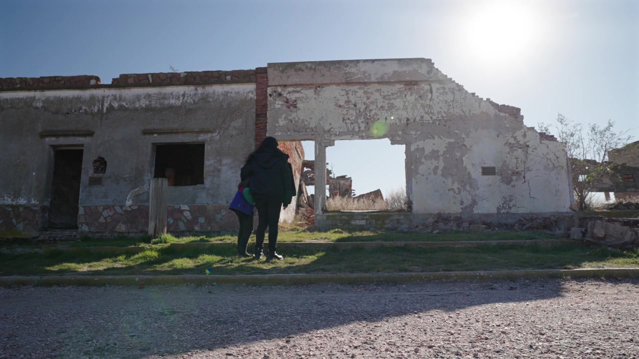 Madre e hija observando ruinas de edificios abandonados en un pueblo desolado y en ruinas en la naturaleza.