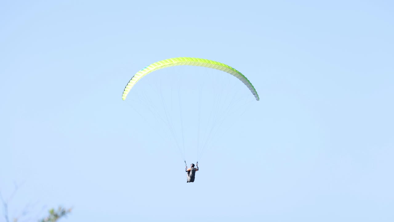 Solo paraglider flying against a clear blue sky