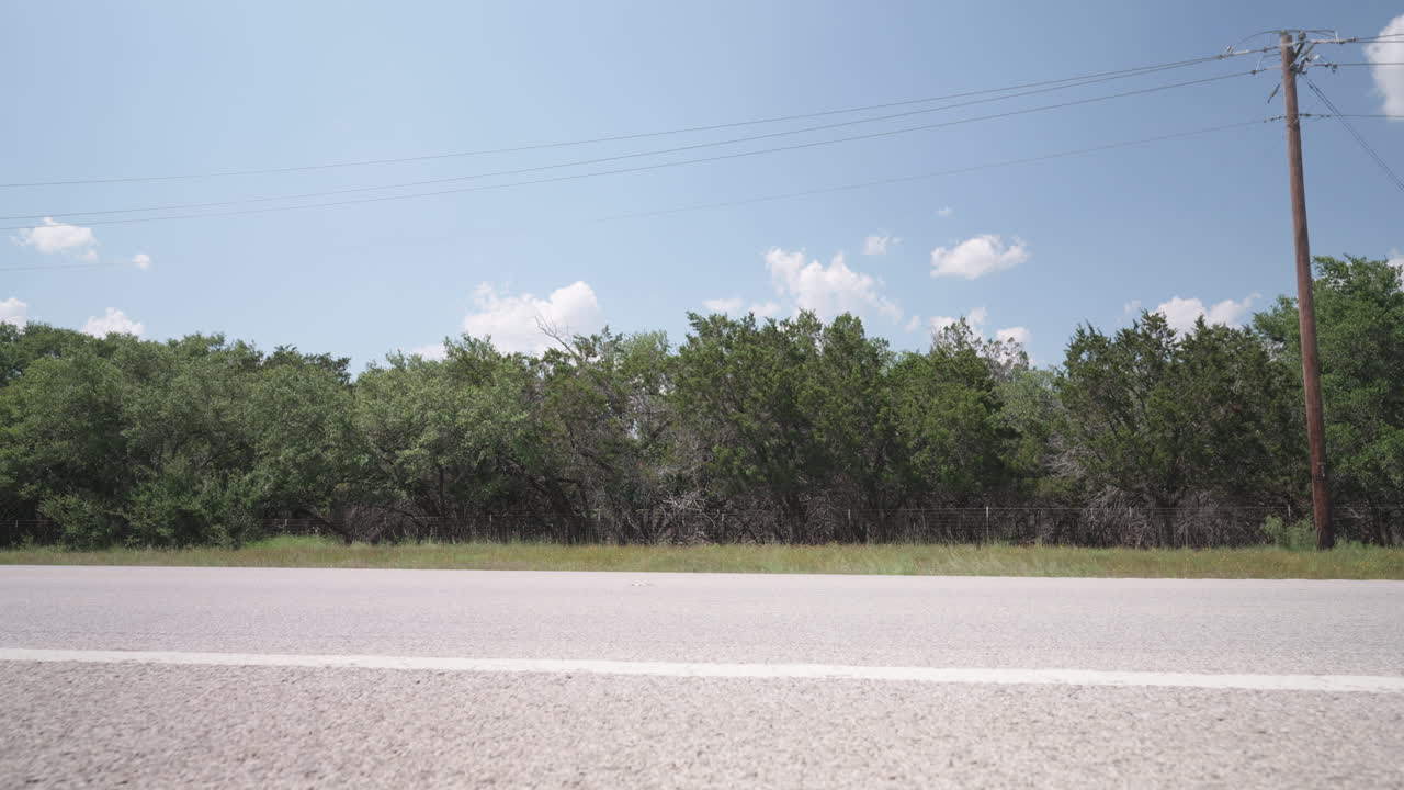 Cars drive past on a sunny highway in the Texas Hill Country - slider left to right