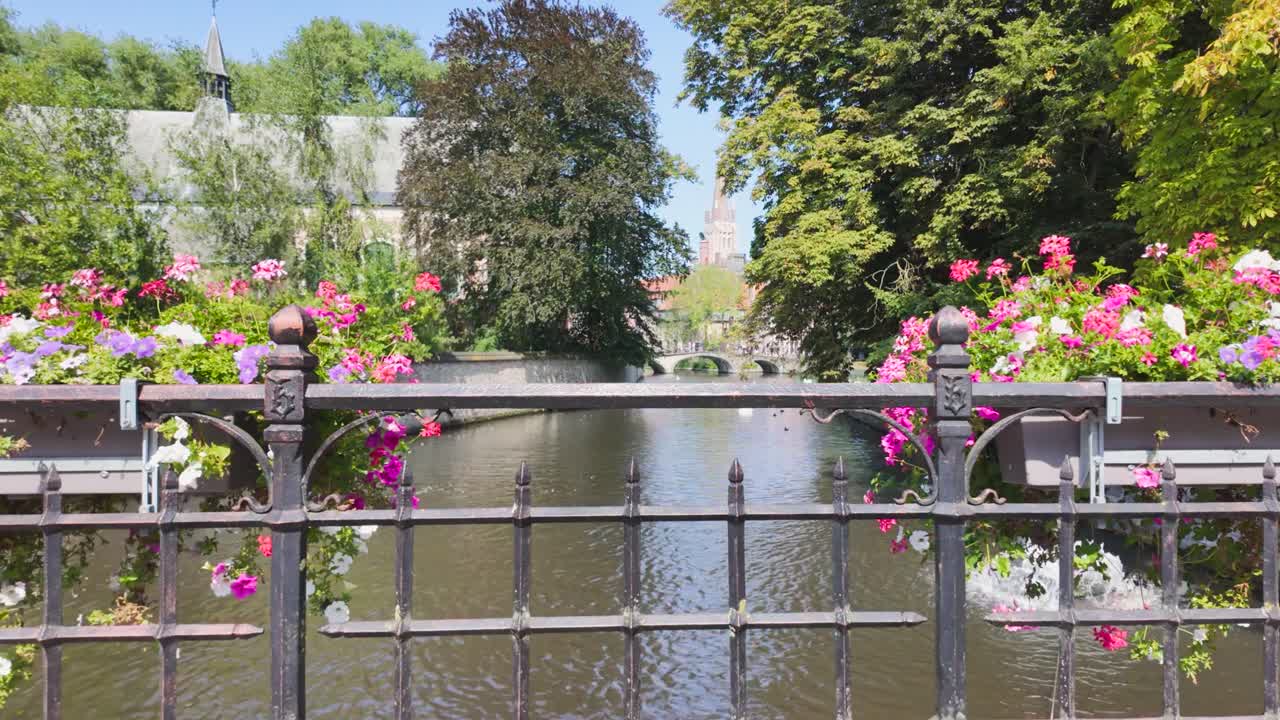 A charming canal bridge with vibrant flowers and lush trees in Bruges, Belgium on a sunny day