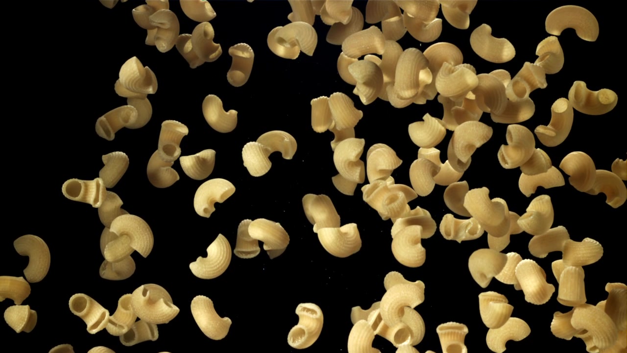 Pasta maccheroni secca che cade al rallentatore su sfondo nero.