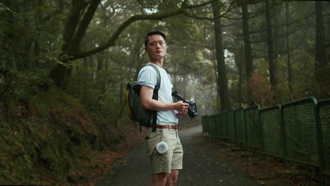 a young asian male photographer in a white t-shirt and a backpack is taking photographs of nature in the forest, located in taiwan