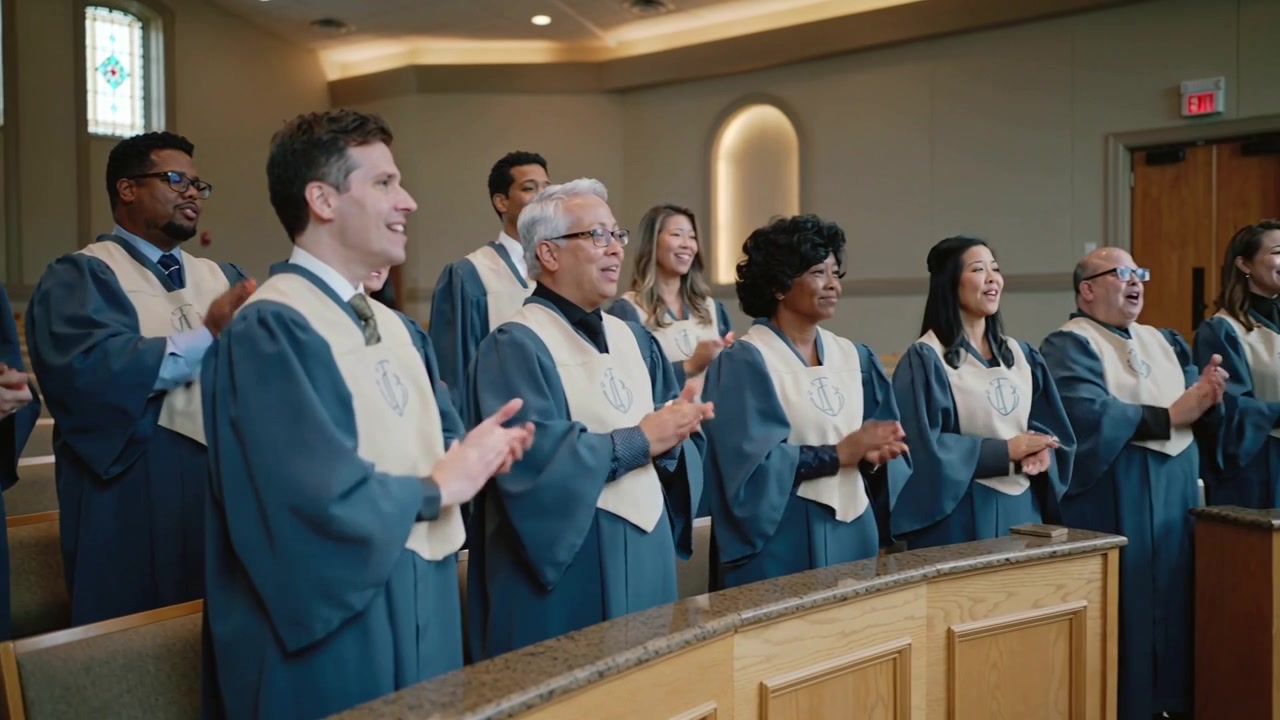 Klappende kor, etter dirigentens tegn, synger foran i kirken i blå kapper med lyse stolaer.