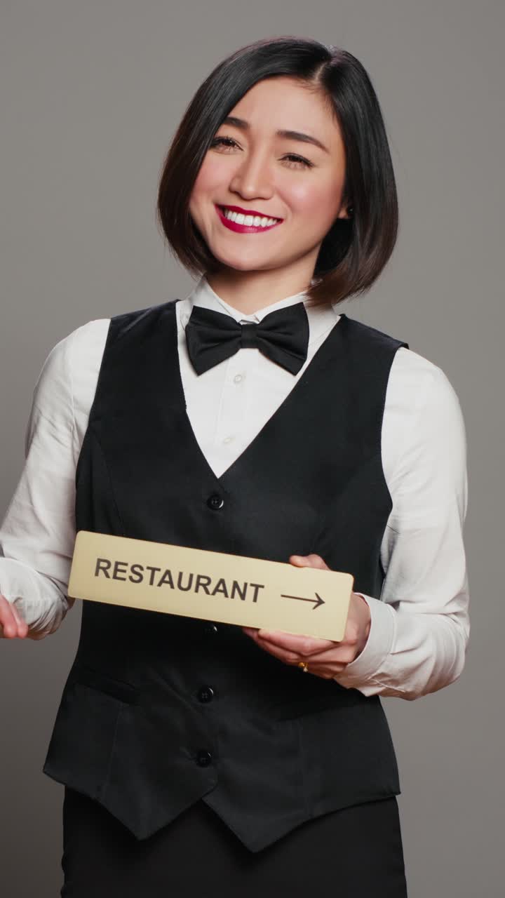 Video verticale: concierge asiatico di un hotel che regge un cartello del ristorante per indicare la direzione