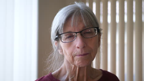 An-old-caucasian-woman-with-aging-face-wrinkles-gray-hair-and-glasses-looking-at-camera-hopeful,-calm-and-peaceful