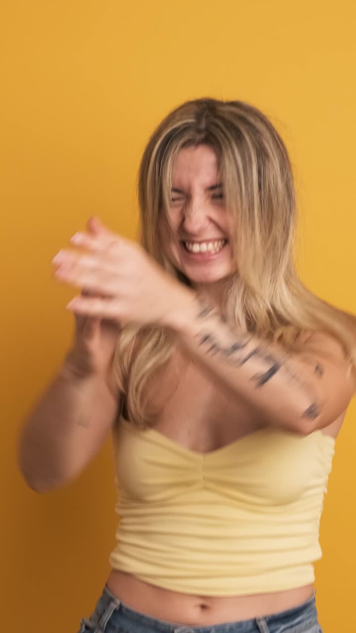 Giovane donna sorridente che salta con le mani alzate su sfondo giallo.