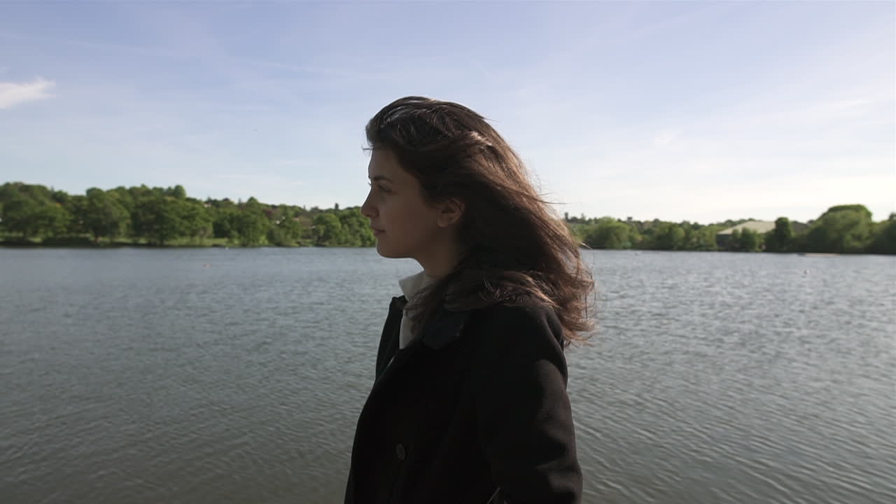 retrato al atardecer de una adorable y hermosa modelo italiana caminando junto a un lago, usando un abrigo negro, mirando a su alrededor, deambulando y siendo libre