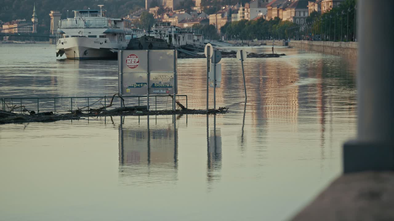 Flooded riverside with partially submerged signs and boats docked in the distance, Budapest, Hungary