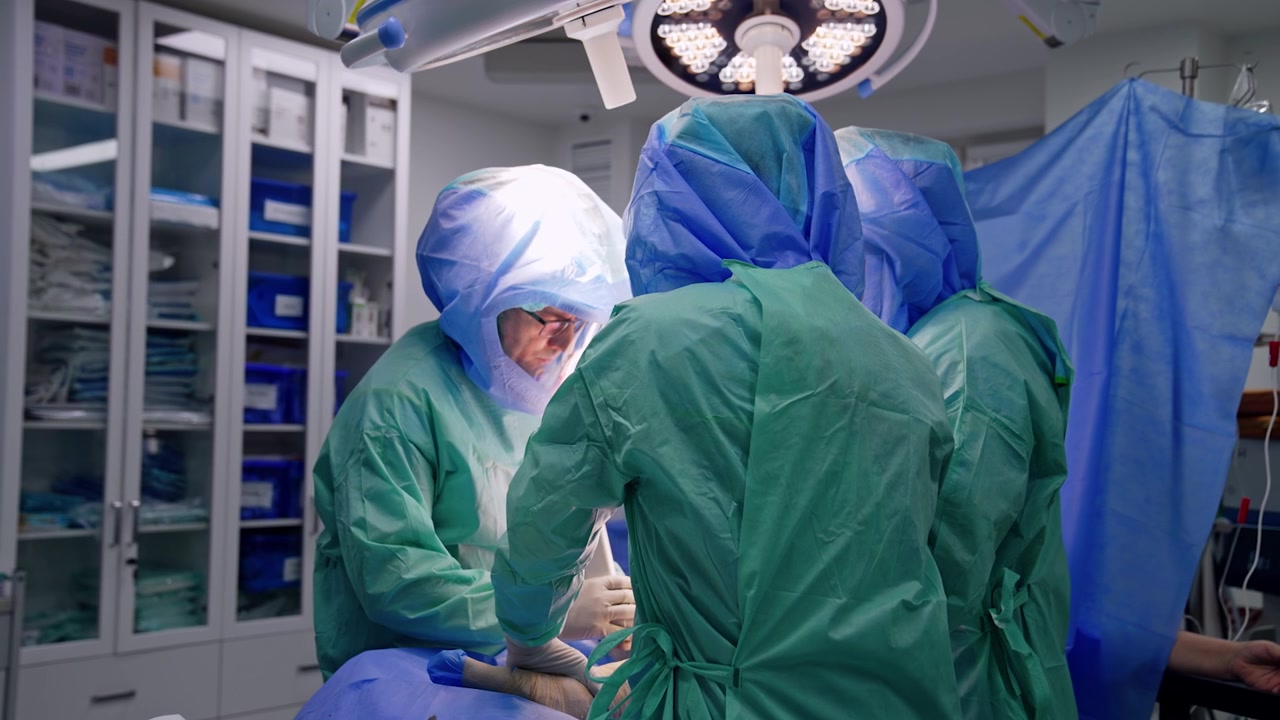 Chirurghi in camici e caschi operano un paziente sotto lampade rotonde. Intervento di chirurgia traumatologica in cliniche moderne.
