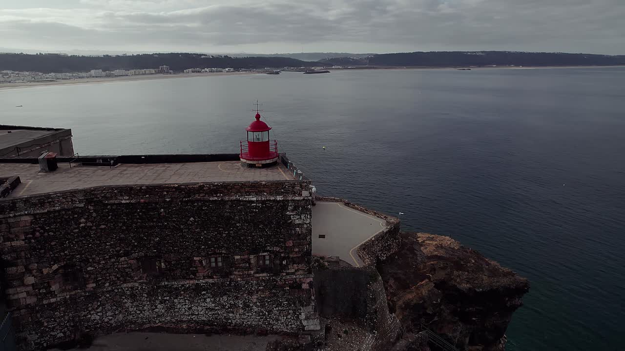 Ripresa aerea orbitante con drone del faro del Forte de São Miguel Arcanjo, che rivela l'orizzonte dell'Oceano Atlantico e la famosa costa per il surf con onde giganti di Praia do Norte a Nazaré, Portogallo.
