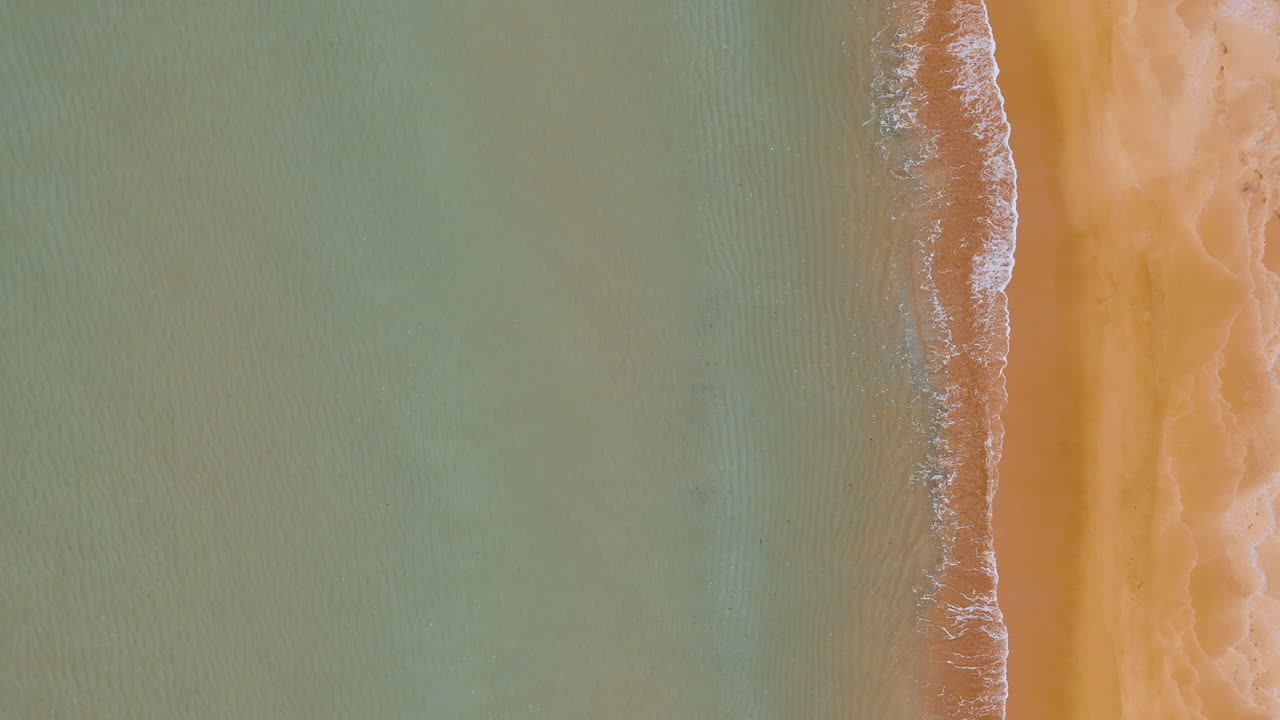 Vista aerea di litorale e sabbia. Scatto minimalista zenitale di acqua di mare che incontra la spiaggia sabbiosa con increspature.