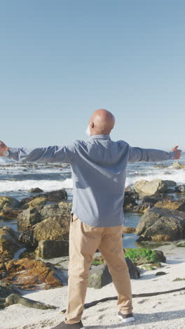 vertical video of senior african american man widening arms at beach, slow motion