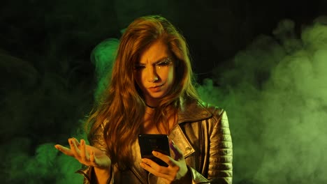 retrato de una joven hermosa y molesta que está enviando mensajes de texto y luego muestra indignada un teléfono inteligente con una pantalla azul. clave de croma para la cámara.