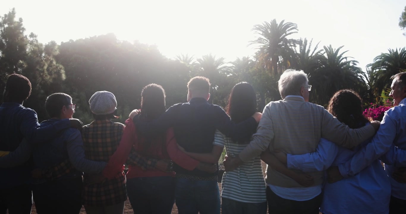 Gruppo eterogeneo di persone che si abbracciano all'aperto al tramonto