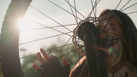 dama tocando suavemente la rueda de su bicicleta, sonriendo suavemente mientras la luz del sol se refleja en ella y la rueda giratoria, creando una atmósfera serena, con un fondo borroso de exuberante vegetación