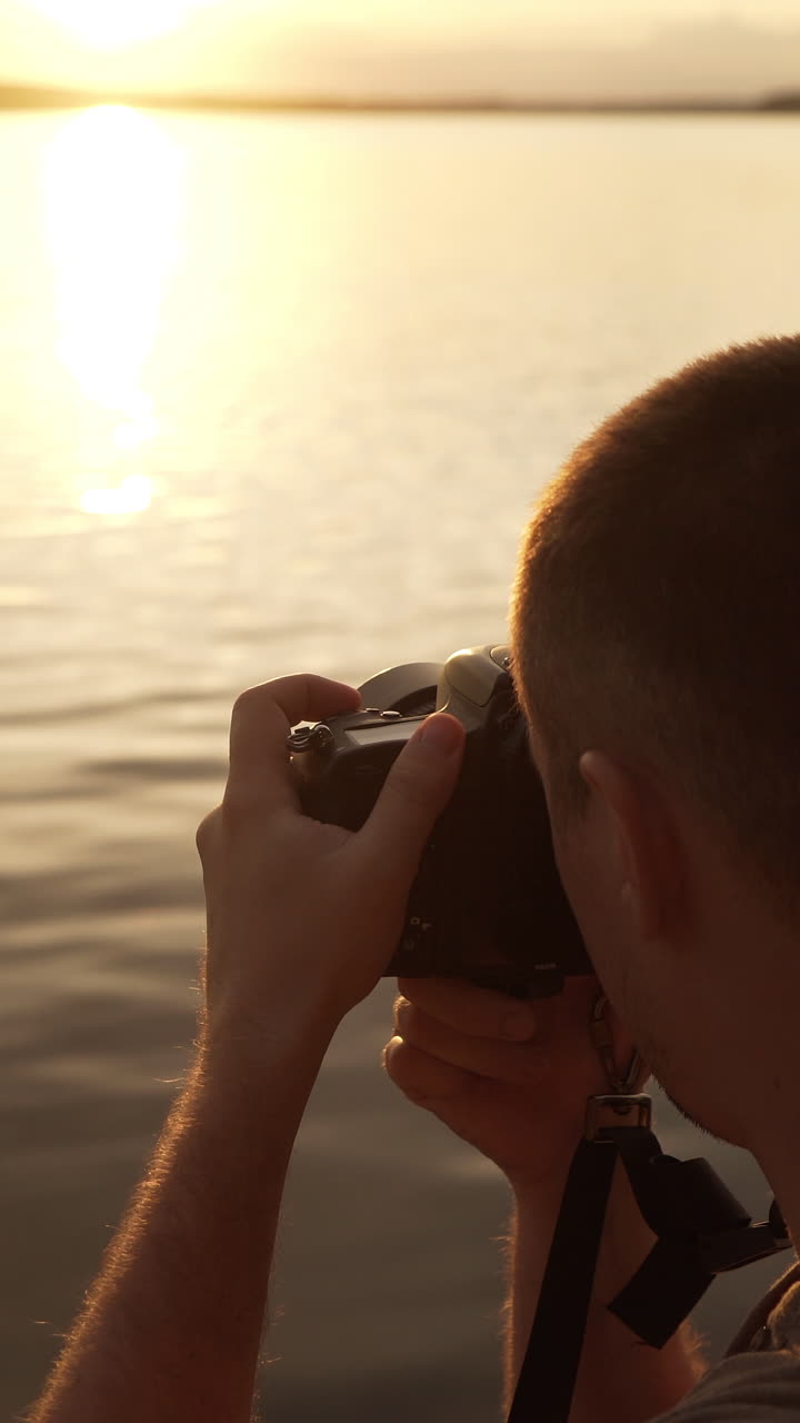 Tourist is photographed on the beach of people swimming in the river at sunset. Vertical video