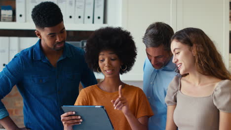 Multi-Cultural-Business-Team-Meeting-In-Office-Looking-At-Digital-Tablet