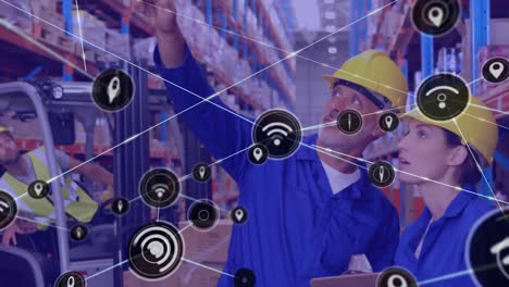 Animation-of-network-of-icons-over-caucasian-male-and-female-worker-checking-stock-at-warehouse