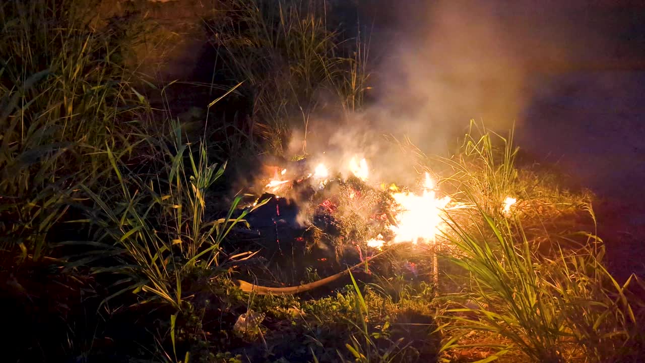 Smoky fire burning of dry grass and garden debris on grass in darkness of night