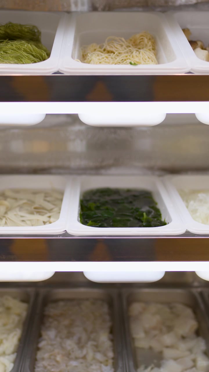 Noodles crudi assortiti e verdure in vassoi sotto luci intense in un buffet asiatico di hotpot