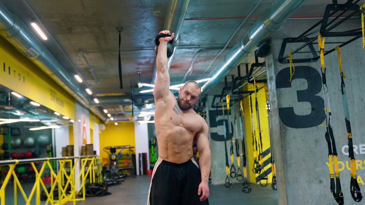 Uomo muscoloso che solleva un kettlebell sopra la testa in una palestra moderna