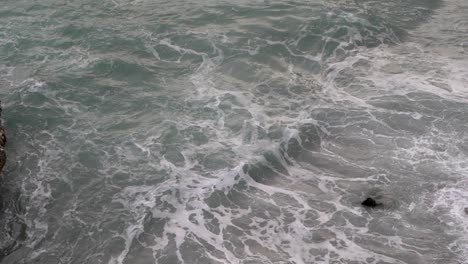 High-above-view-down-towards-rough-sea-with-waves-breaking-against-rocks