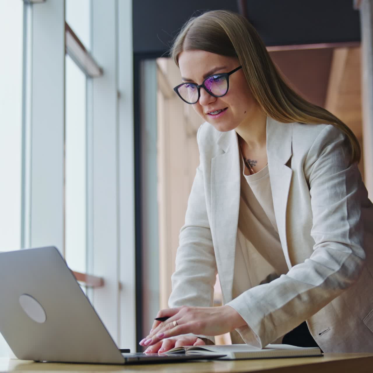 Office lady surfing the net and taking notes. Female employee standing leaned on the table in a spacious office