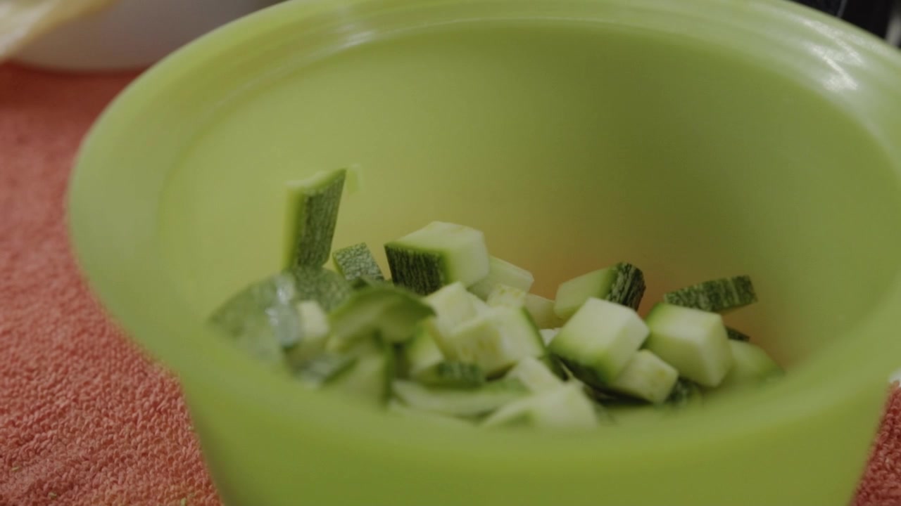 Vista ravvicinata di pezzi di zucchine a cubetti posti all'interno di una ciotola, verdura fresca e verde preparata per la cottura con una consistenza pulita e un semplice allestimento da cucina