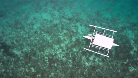 Bangka-boat-floating-on-crystal-clear-tropical-water,-drone-shot