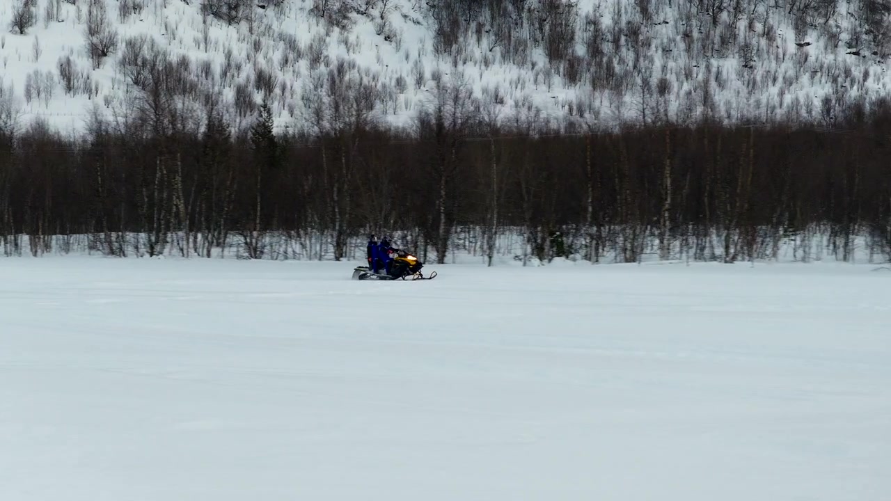 Norveç, Tromso'nun karlı vahşi doğasında ilerleyen bir kar motosikletinin havadan görünümü. Donmuş bir manzara ortamında Arktik macerayı ve kış turizmini vurguluyor.