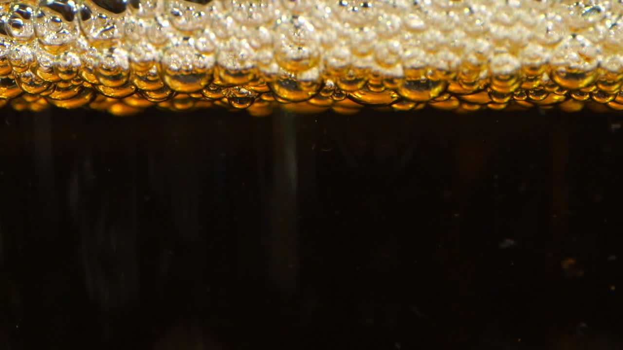 Big bubbles that burst on the top of a glass in a yellow liquid like beer cider or lemonade