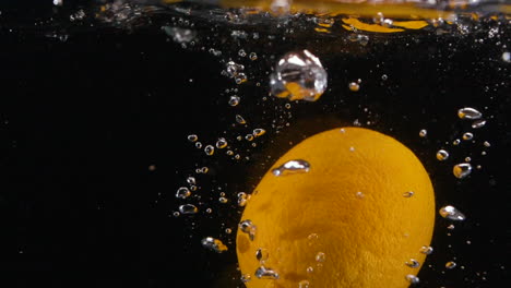 Cámara-Lenta-Dejando-Caer-Frutas-Cítricas-En-Agua-Para-Una-Bebida-Refrescante-Con-Limón-Naranja-Lima