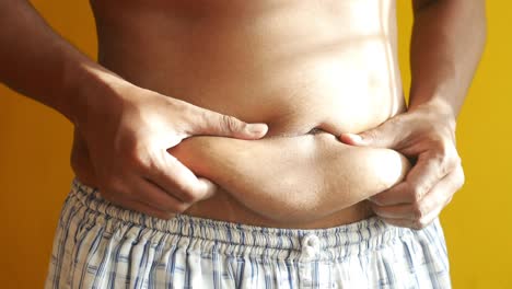 mans hand holding excessive belly fat, overweight concept