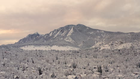 High-drone-shot-moving-left-of-Boulder-Colorado-and-rocky-Flatiron-mountains-after-large-winter-snow-storm-covers-trees,-homes,-streets,-and-neighborhood-in-fresh-white-snow