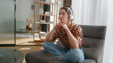 woman sitting cross-legged on chair wearing headphones listens to podcast