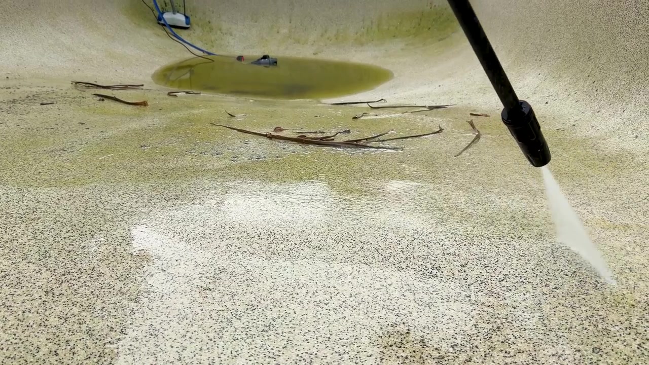 En højtryksrenser fjerner grønne alger og snavs fra en betonpooloverflade i slow-motion.