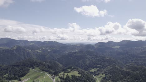 Frontales-Drohnenvideo,-Das-Sich-über-Häuser-Im-Triglav-Bewegt,-Mit-Hügeln-Am-Horizont-Und-Klarem-Himmel-Mit-Wolken