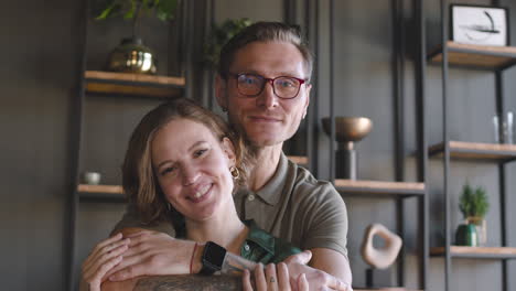 Portrait-Of-A-Happy-Couple-Smiling-At-Camera-At-Home-While-Man-Embracing-Woman-From-Behind