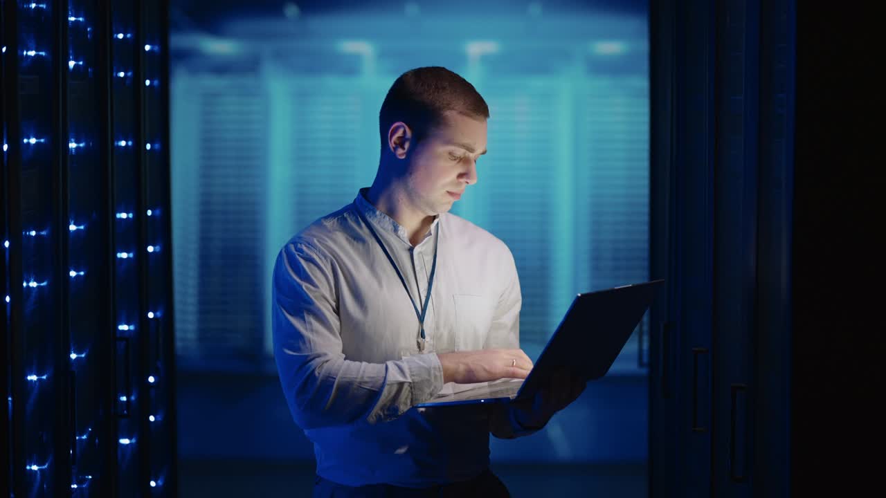 Concept of Digitalization of Information: IT Specialist In front of Server Racks with Laptop, Activates Data Center with a Touch Gesture. Working on a Laptop Standing Before Open Server Rack Cabinet